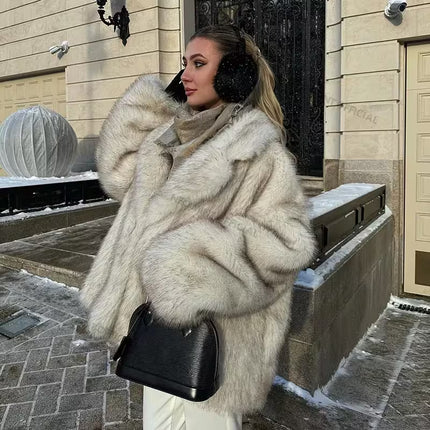 Woman in a fur coat and black ear muffs standing on a snowy street.