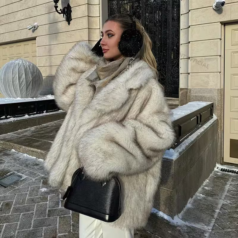Woman in a fur coat and black ear muffs standing on a snowy street.