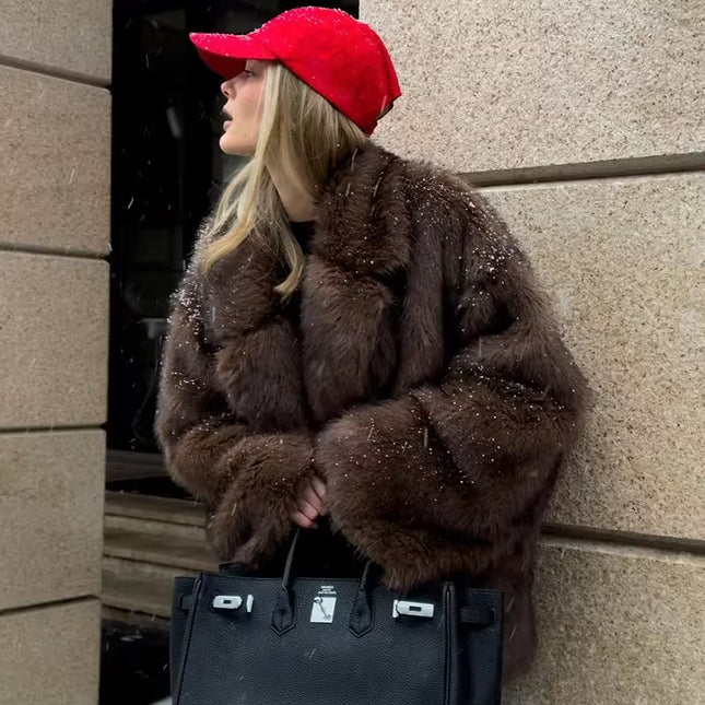 Person wearing a brown fur coat and red cap leaning against a stone wall.